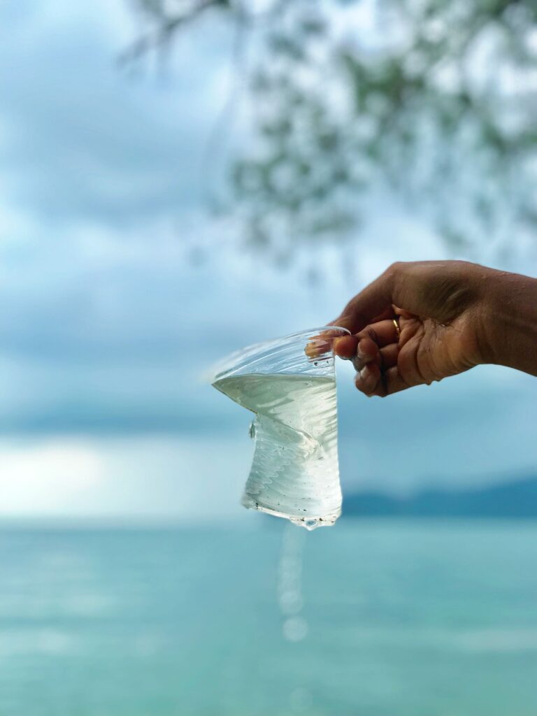 Someone holds a plastic cup dripping water, with a beautifull blue ocean background.