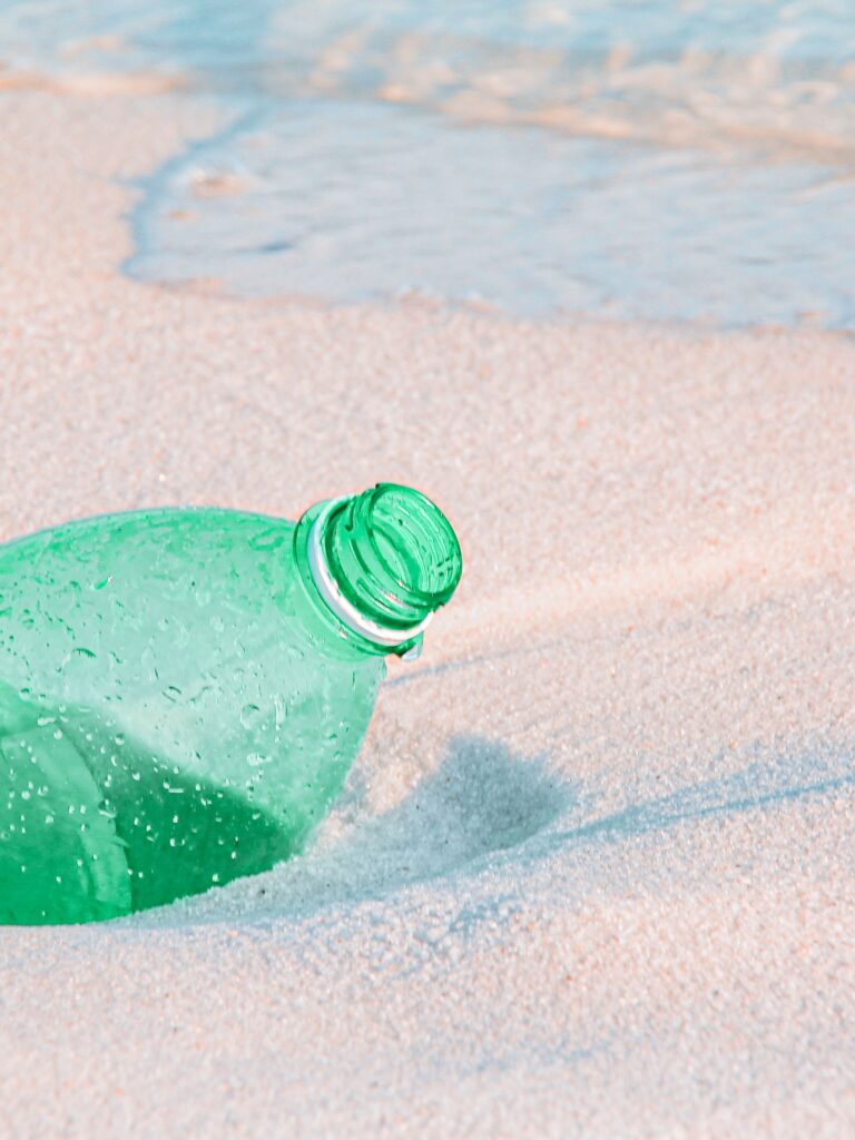 Empty plastic bottle half burries in the sand by the sea.